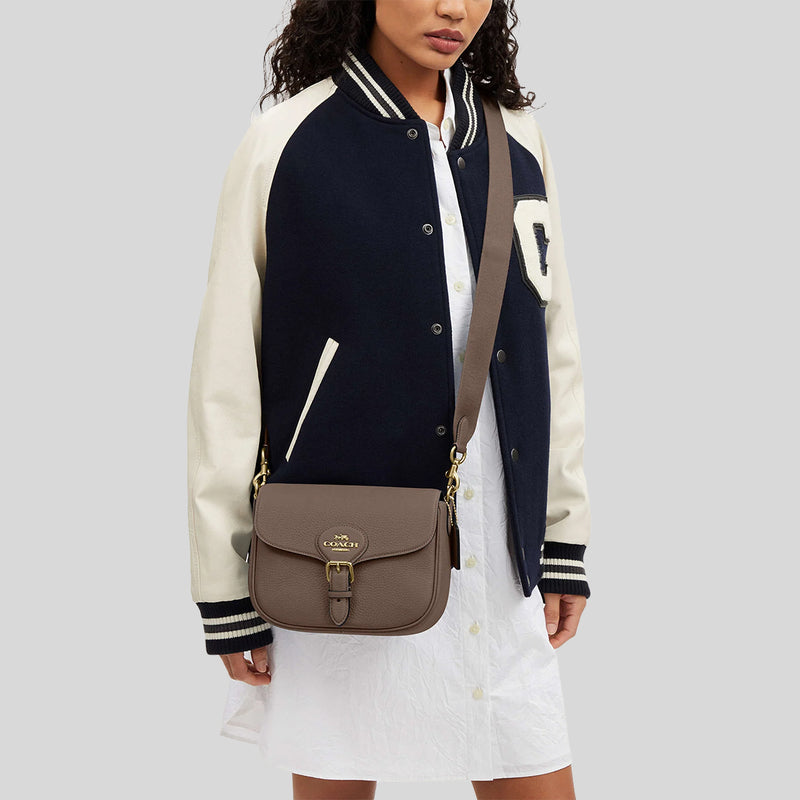 Person wearing a navy and white varsity jacket with a brown bag on a light gray background